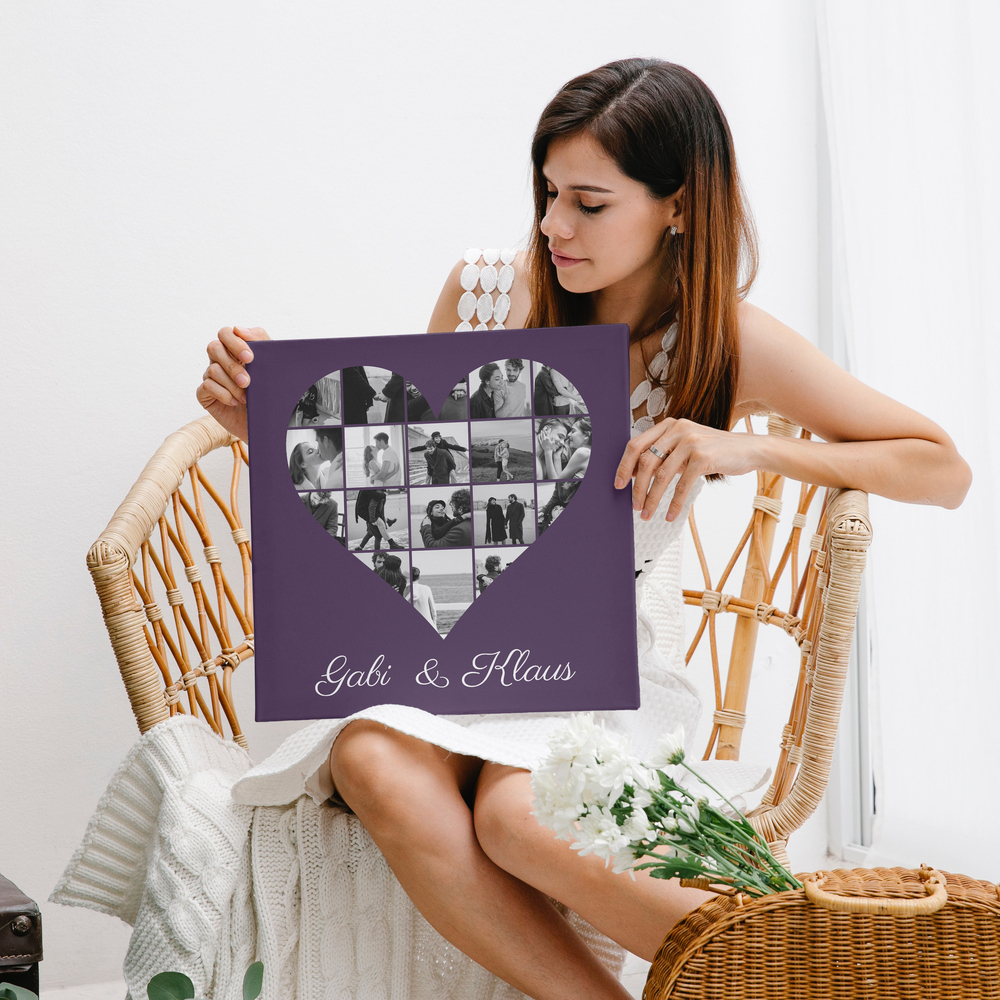 Tela con collage di foto in bianco e nero a forma di cuore e nomi su fondo viola, davanti a una poltrona in rattan