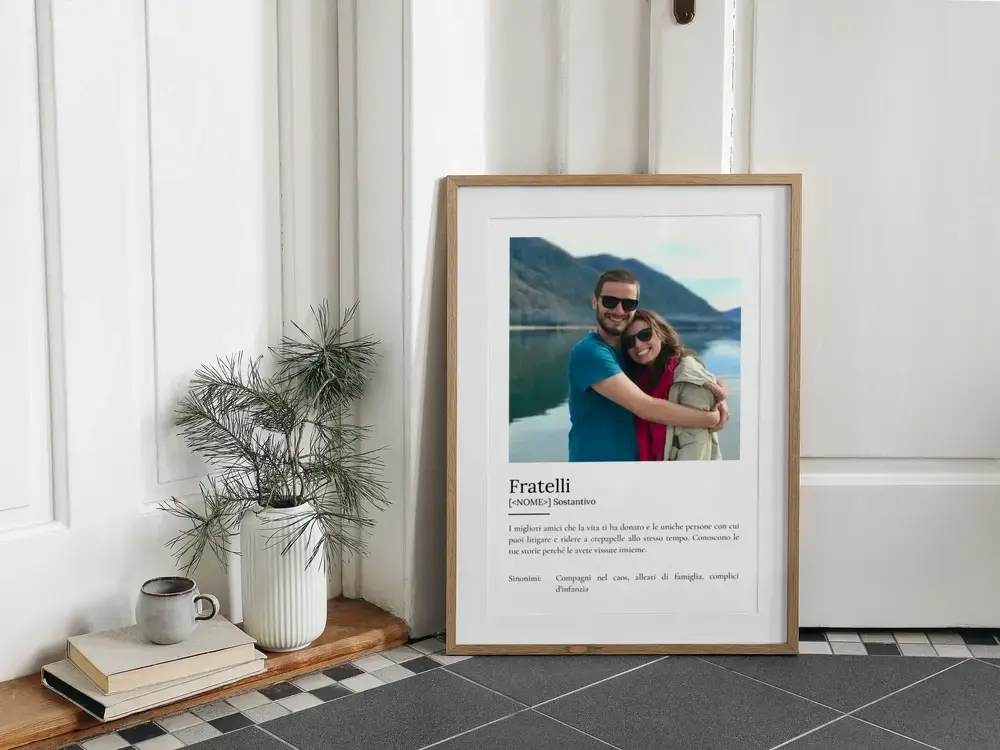 Poster con foto di fratello e sorella e definizione, in cornice di legno appoggiata a terra accanto a una pianta