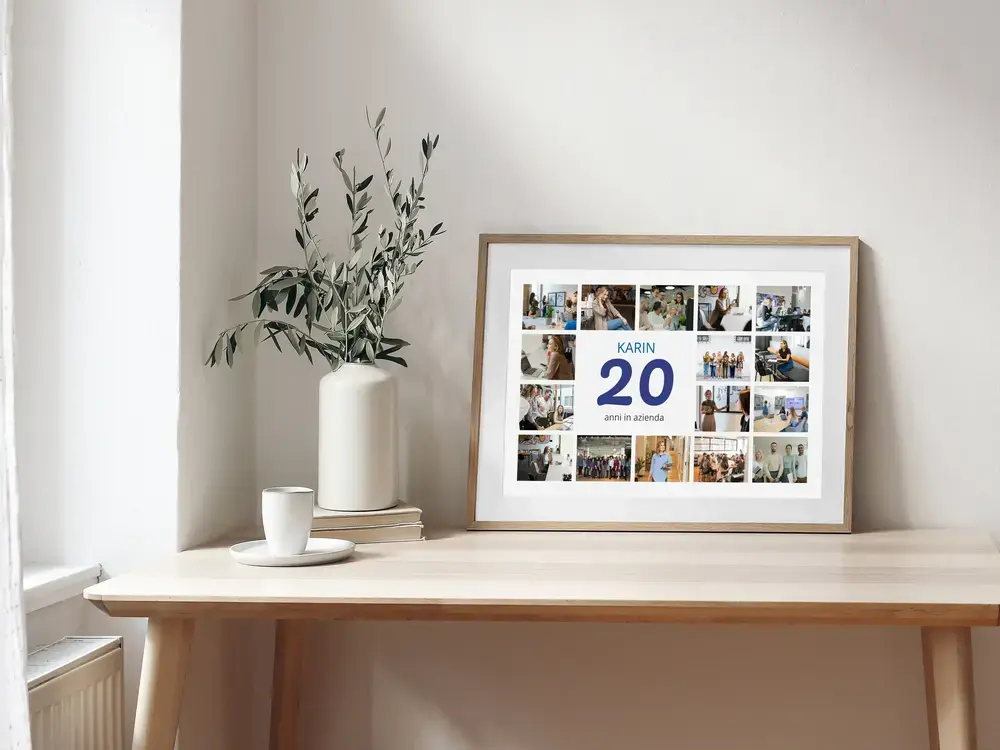 Collage fotografico per 20 anni in azienda, con nome e numero blu, in cornice di legno sulla scrivania accanto a un vaso
