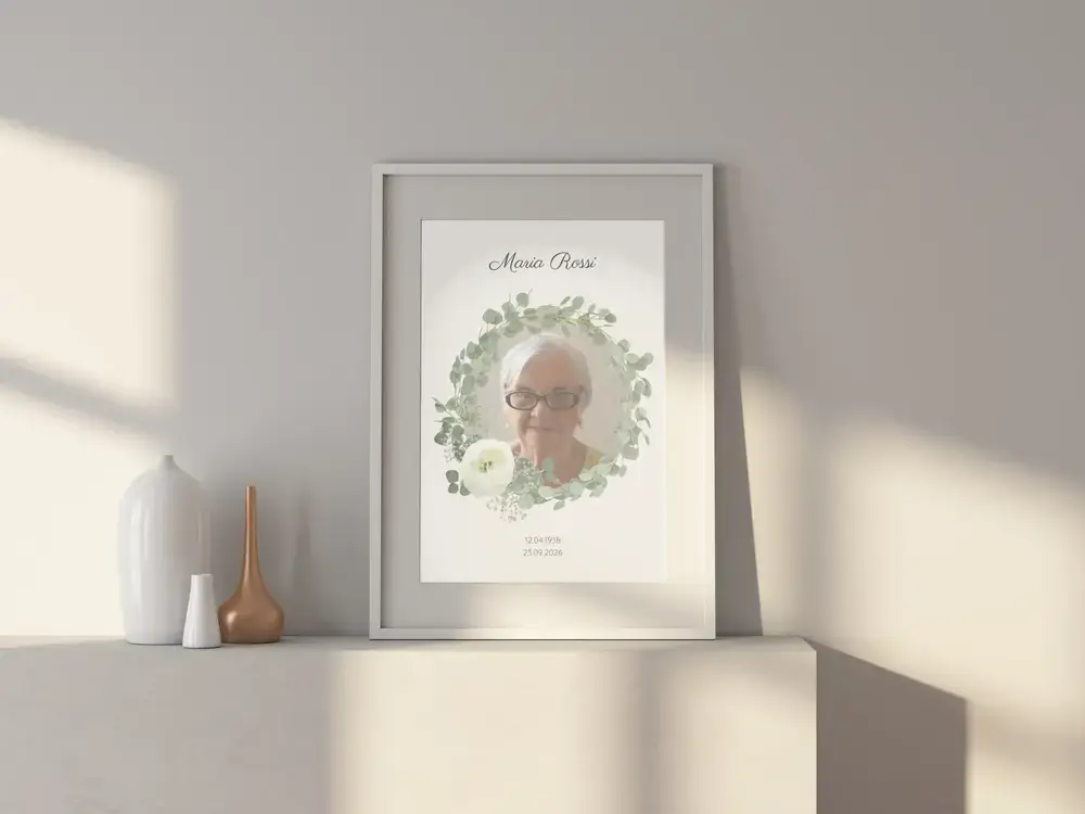 Quadro commemorativo con ritratto e ghirlanda di eucalipto, in cornice chiara su una credenza bianca accanto a vasi