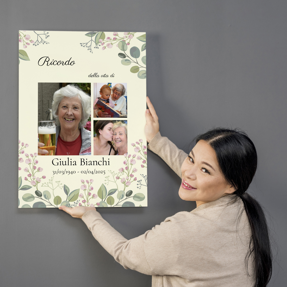 Tela commemorativa con tre foto, nome e fiori su fondo verde chiaro, presentata su una parete grigia.